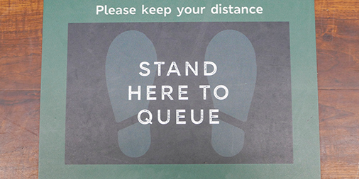 Floor sticker on a wooden floor. Customers are asked to keep their distance.