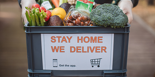 A person holding a box of food with "Stay home we deliver" sticker.