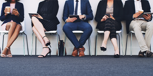 Group of business people sitting on chairs in a line using tablets and smartphones, cropped shot