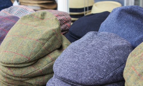Variation men's newsboy cap stack in clothing store. Large group of hats are placed in a row, stack together. Many different textured & pattern.