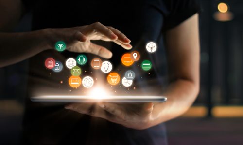 A person holding a tablet with icons emerging from it, representing various applications