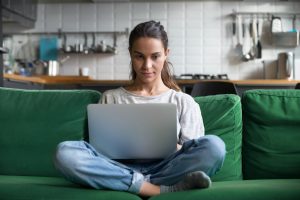 Serious woman using laptop checking email news online sitting on sofa, searching for friends in internet social networks or working on computer, writing blog or watching webinar, studying at home