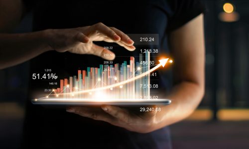 Businessman holding tablet and showing a growing virtual hologram of statistics, graph and chart with arrow up on dark background. Stock market. Business growth, planing and strategy concept.