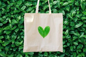 Blank white mockup linen cotton tote bag on green bush trees foliage background. Heart logo from leaves. Nature friendly style. Environmental conservation recycling plastic free