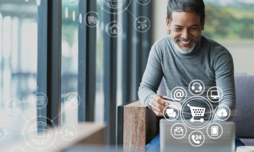 A man holding bank card and using a laptop with shopping icons floating in air