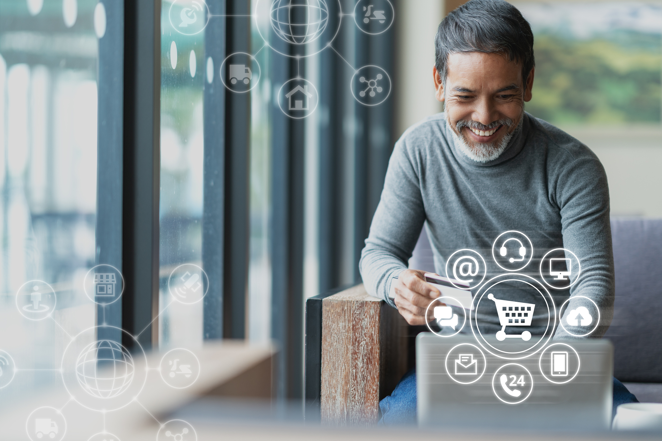 A man holding bank card and using a laptop with shopping icons floating in air