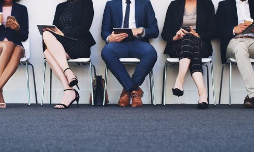 Group of business people sitting on chairs in a line using tablets and smartphones, cropped shot
