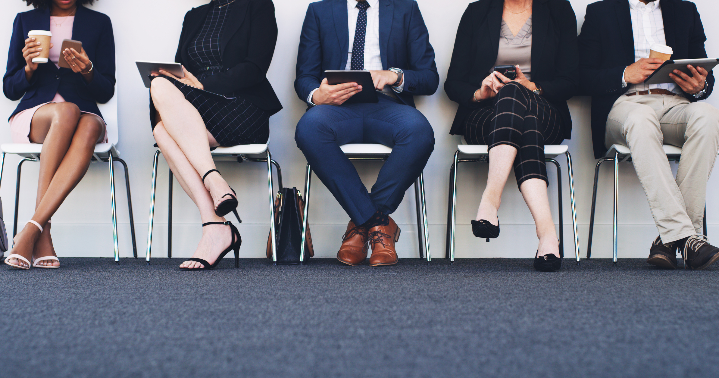 Group of business people sitting on chairs in a line using tablets and smartphones, cropped shot