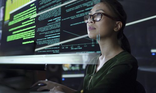 Stock photo of a young Asian woman looking at see through data whilst seated in a dark office