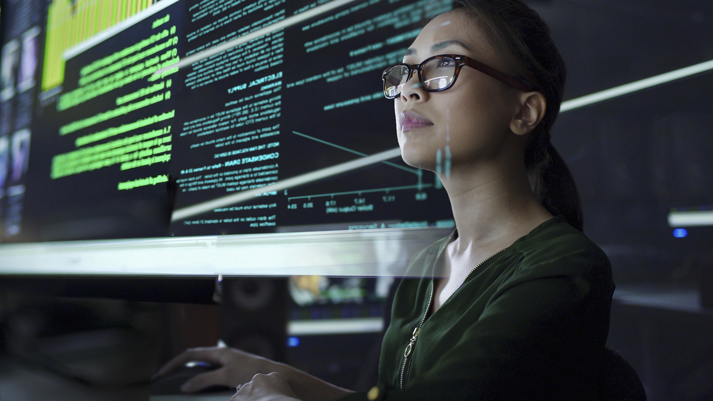 Stock photo of a young Asian woman looking at see through data whilst seated in a dark office