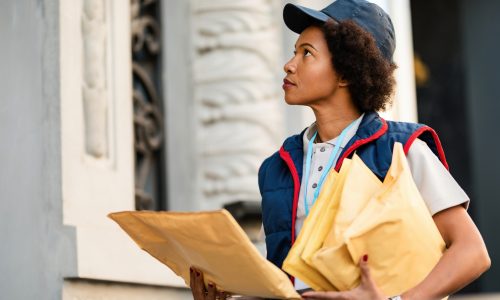 Black postwoman delivering mail in residential district.