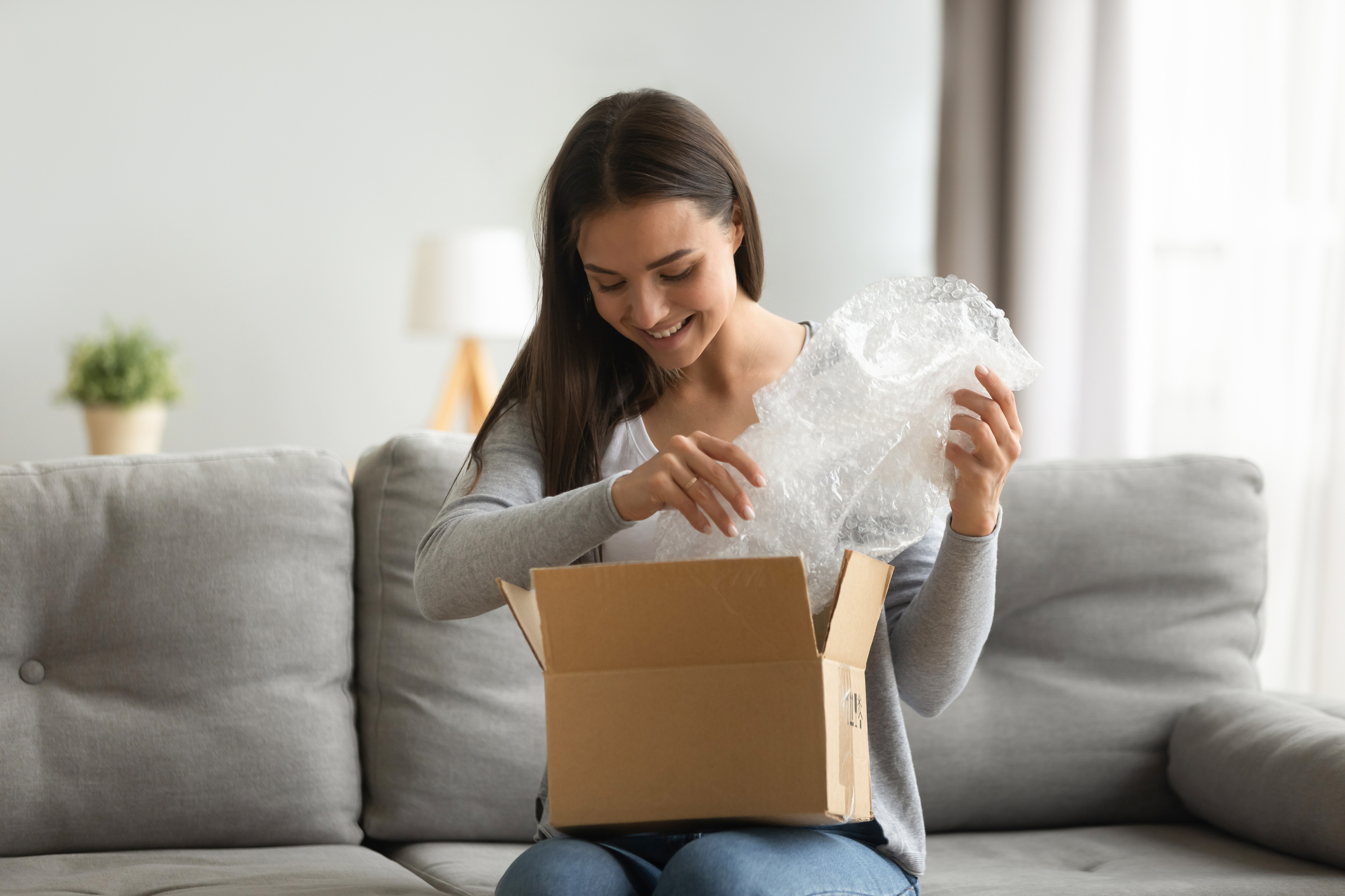 Happy woman opening parcel box on sofa at home