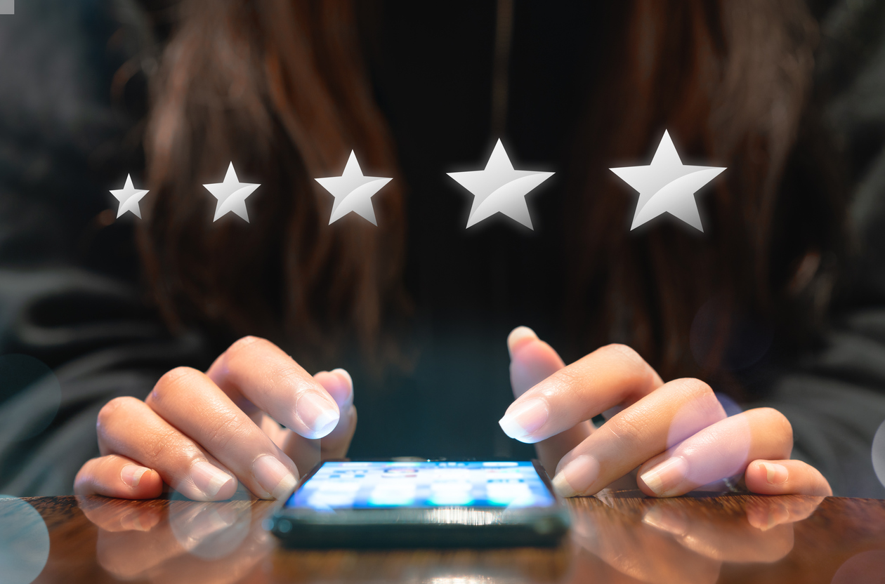Hands of young woman over mobile smartphone with five silver graphic stars above.
