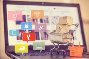 Box / carton with shopping cart, a grocery basket on a laptop keyboard, depicts consumers / customers / buyer buy goods and service from office or home