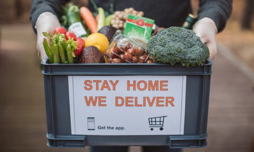 A person holding a box of food with "Stay home we deliver" sticker.