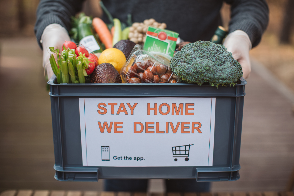 A person holding a box of food with "Stay home we deliver" sticker.