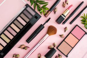 Lipstick, nail polish, eye shadows and blush, brushes and pencils staged on pink table