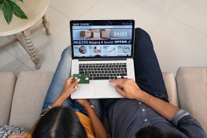 Top view of indian couple doing shopping online on website with laptop at home. High angle view of man and woman using laptop on legs and paying with credit card. Indian casual couple selecting product on ecommerce portal on computer.