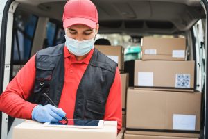 Delivery man in red clothes wearing gloves and mask writing signing on tablet