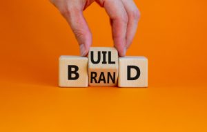 Build your brand symbol. Businessman turns wooden cubes and changes the word 'build' to 'brand'. Beautiful orange background. Build your brand and business concept. Copy space.