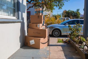 Amazon packages piled up in a huge pile outside a home with car in the background
