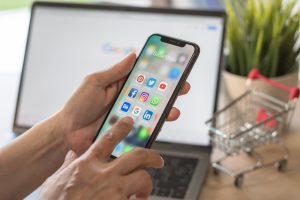 Hand with a phone with social media app multi-channel icons on screen.